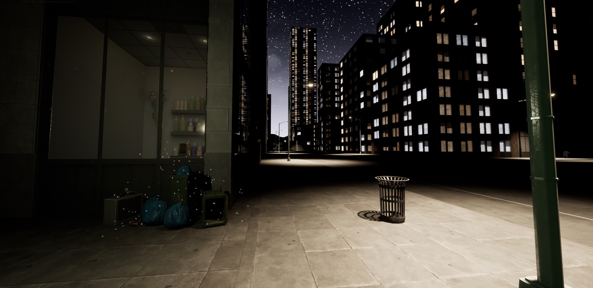 A dark street at night with a lamp post, a trash can on the sidewalk and a lit shopfront to the left.